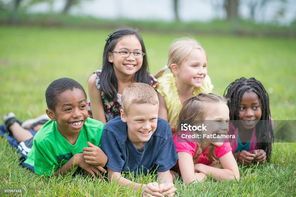 Children Relaxing at the Park A multi-ethnic group of elementary age children are lying in the grass in a dog pile and are smiling while looking at the camera. African Ethnicity Stock Photo