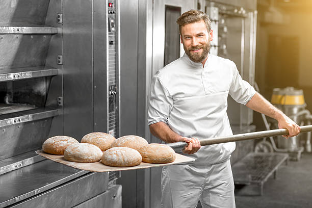 Baker taking out from the oven baked buckweat bread Handsome baker in uniform taking out with shovel freshly baked buckweat bread from the oven at the manufacturing baking bread stock pictures, royalty-free photos & images