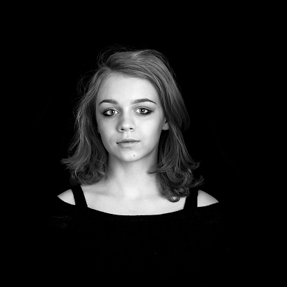 Black and white portrait of beautiful teenage Caucasian blond girl over black background