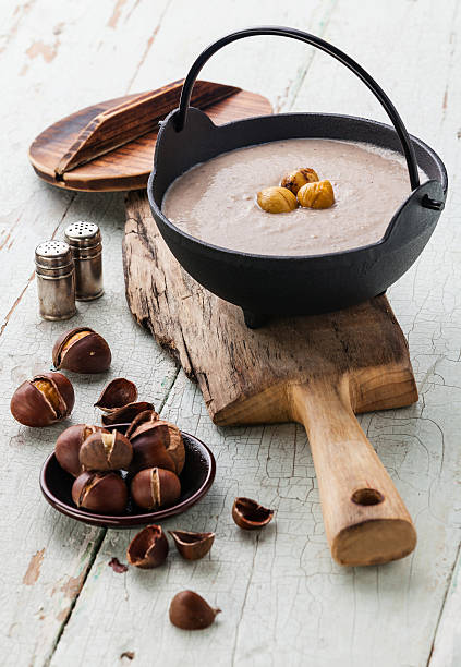 Chestnut soup Chestnut soup in black iron pot with roasted chestnuts on blue textural background cream soup stock pictures, royalty-free photos & images