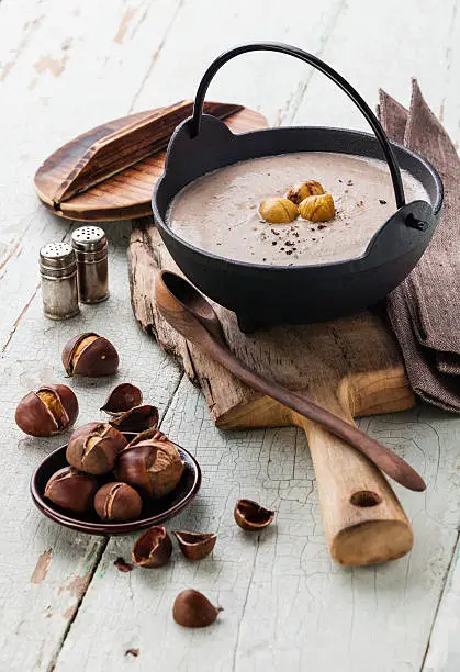 Chestnut soup in black iron pot with roasted chestnuts on blue textural background