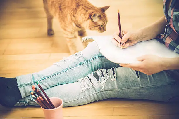 Young blonde woman relaxing at home by coloring book-close up. Adult Coloring Books; GInger cat on the wooden floor looking. Slovenia, Europe. Side view, copy space. Nikon D800, full frame, Nikkor 105mm, aperture 2.8.