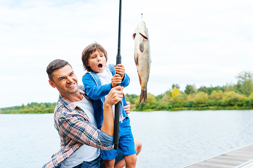Happy boy holding big fish, and showing it to his father, while they are on the boat