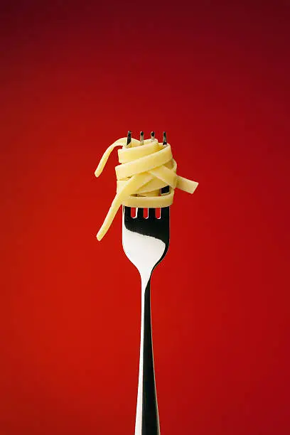 Pasta with silver fork on red background.