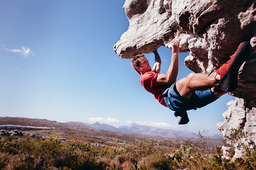 Rock climber holding on to rock overhang as he boulders up mountain. He is strong and focussed.