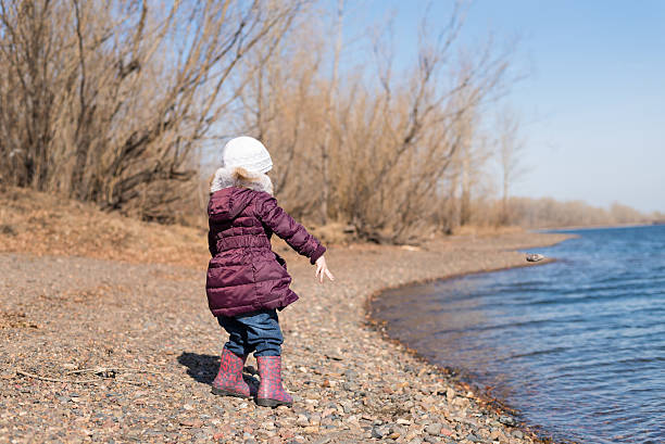 Girl throwing stones into river Little girl throwing stones into river in spring backside for a girl on the beach stock pictures, royalty-free photos & images