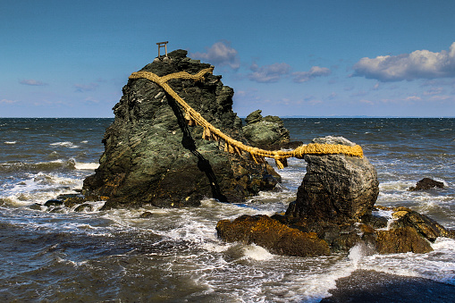 Meoto Iwa, or the Married Couple Rocks, are a couple of small rocky stacks in the sea off Futami, Mie, Japan. They are joined by a shimenawa (a heavy rope of rice straw) and are considered sacred by worshippers at the neighboring Futami Okitama Shrine (Futami Okitama Jinja). According to Shinto, the rocks represent the union of the creator of kami, Izanagi and Izanami. The rocks, therefore, celebrate the union in marriage of man and woman. The rope, which weighs over a ton, must be replaced several times a year in a special ceremony. The larger rock, said to be male, has a small torii at its peak.