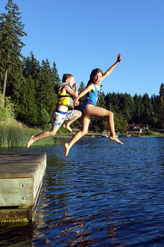 Picture of a boy and girl jumping from floating dock into St. Mary Lake on Salt Spring Island,BC,Canada.