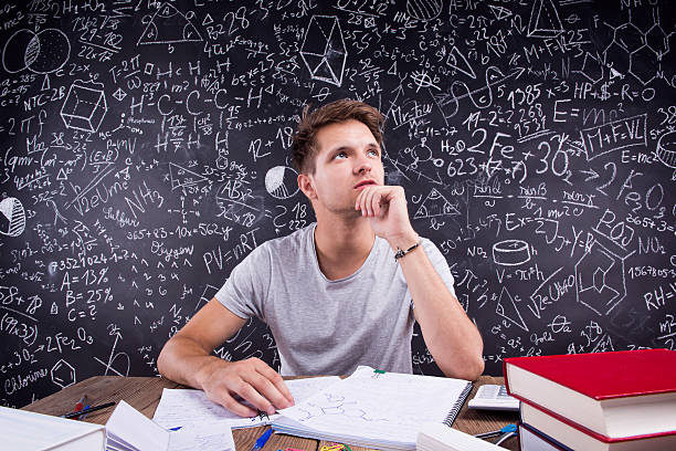 Thoughtful hipster student doing his homework in front of a big blackboard