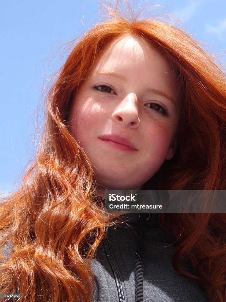 Image of attractive, red haired teenage girl looking-down at camera Photo showing an attractive, red haired teenage girl looking down towards the camera. A clear blue sky can be seen behind the teenager's head with the sun reflecting off the girl's auburn hair. 12-13 Years Stock Photo
