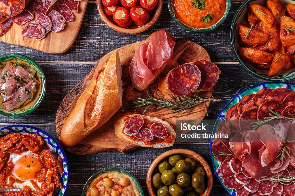 Typical spanish tapas concept, rustic style,  top view. Typical spanish tapas concept. Concept include variety slices jamon,  chorizo, salami, bowls with olives,  peppers, anchovies, spicy potatoes, mashed chickpeas on a wooden table. Tapas Stock Photo