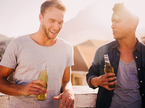 Two young men hanging out after work for a drink on the rooftop of a building at sunset