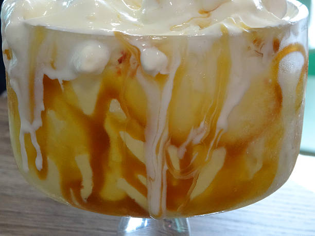 Image of melting toffee fudge sundae, vanilla icecream, toffee sauce Photo showing a toffee fudge sundae, made with vanilla ice cream, fudge pieces and toffee caramel sauce, topped with marshmallows and whipped cream, and served with a chocolate flake and wafer roll. This indulent treat was served in an ice cream parlour. ice cream with wafer rolls stock pictures, royalty-free photos & images
