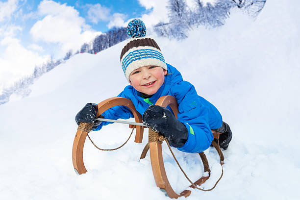 istock Little boy  slide down laying on sledge smile 517130574