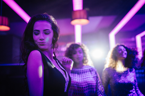 Happy young adult girl dancing with her friends on a night club party