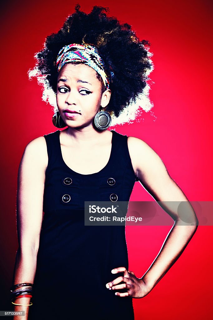 Young woman with wild Afro looks sideways, worried and suspicious A cute young woman with wild Afro-style hair looks to the side, worried, suspicious, and confused. Red background. 20-29 Years Stock Photo