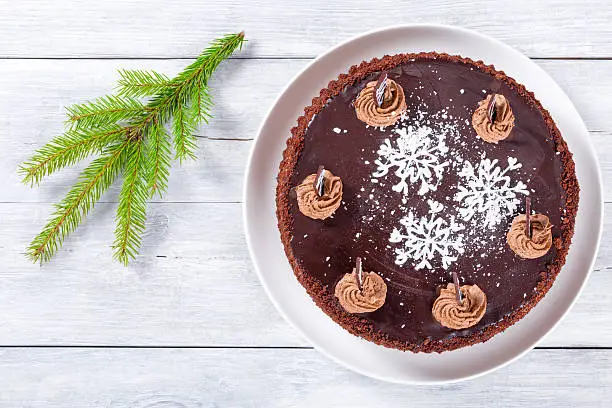 delicious chocolate cake decorated with chocolate chips and icing-sugar snowflake on the white dish, closeupchocolate cake decorated with chocolate chips and icing-sugar snowflake, close-up