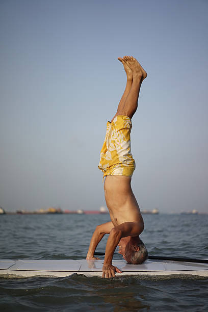 Asian Retiree in his 60s doing headstand on surf board stock photo
