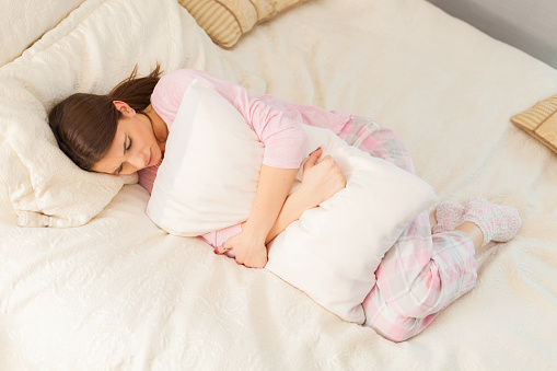 Young woman in bed, embracing a pillow with a grimace on her face