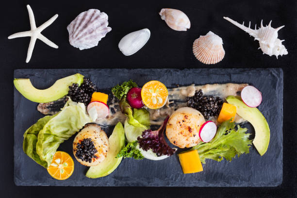Pan seared scallops with salad, avocado, radish, mango and black caviar on a stone plate, top view