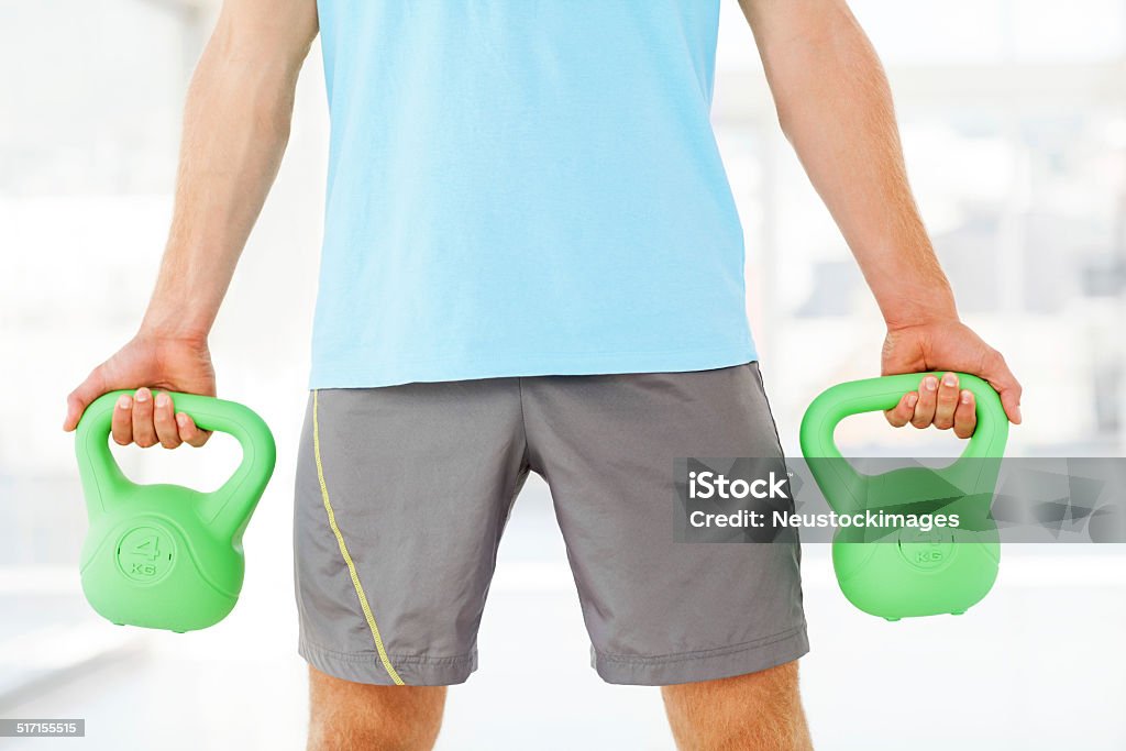 Man Holding Kettle Bells In Gym Midsection of young man holding kettle bells in gym. Horizontal shot. 20-24 Years Stock Photo