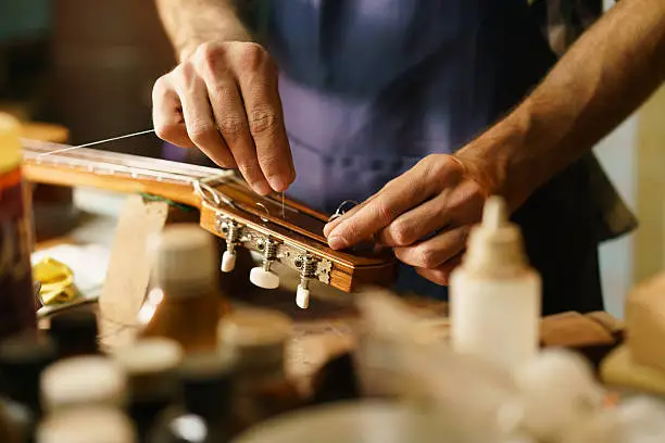 Lute maker shop and classic music instruments: young adult artisan fixing old classic guitar adding a cord and tuning the instrument. Close up of hands and palette