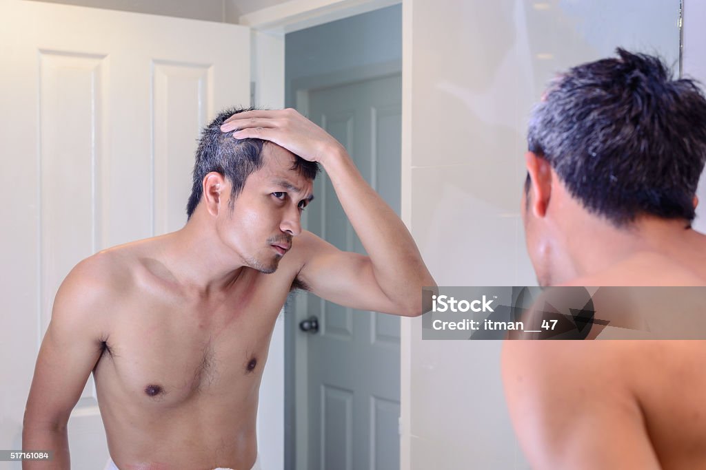 Man worried about gray hair while looking into a mirror. Gray Hair Stock Photo