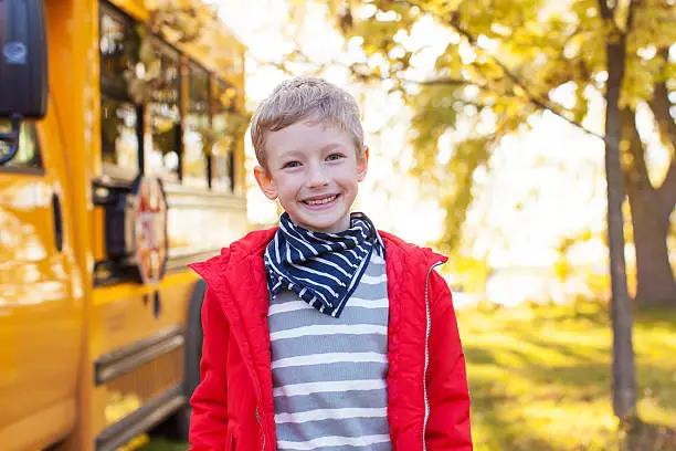 cheerful little boy standing near schoolbus ready to go to school, back to school concept