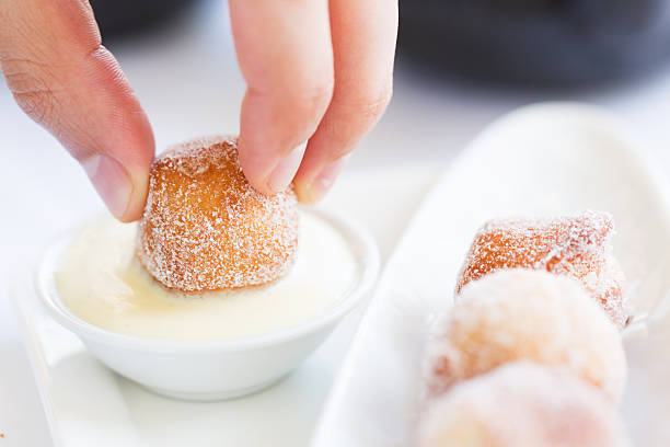 fresh beignets with sauce close-up of person's hand dipping fresh beignet in sauce, traditional new orleans or french cuisine beignet stock pictures, royalty-free photos & images