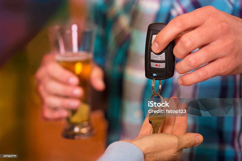 Drinking and Driving.  Man gives car keys to friend.  Beer. Man gives his car keys to a designated driver friend after he has been drinking too much at nightclub.  Beer glass.  Drunk Driving Stock Photo