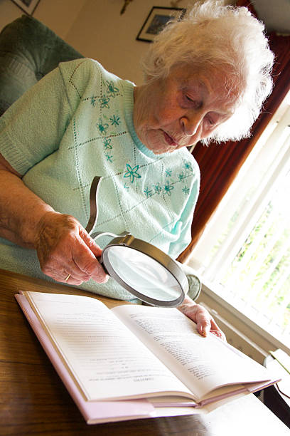 istock Elderly woman using a magnifier to read a book 517170707
