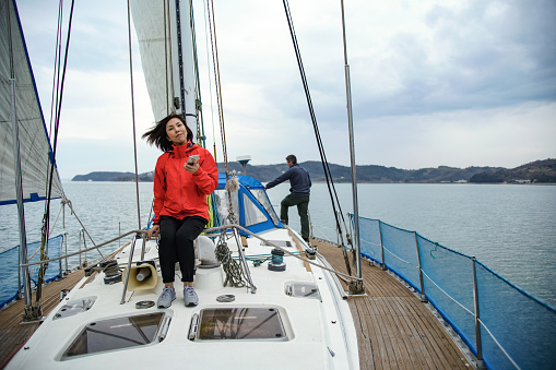 A mid adult woman using smartphone on a yacht while her husband is in the background