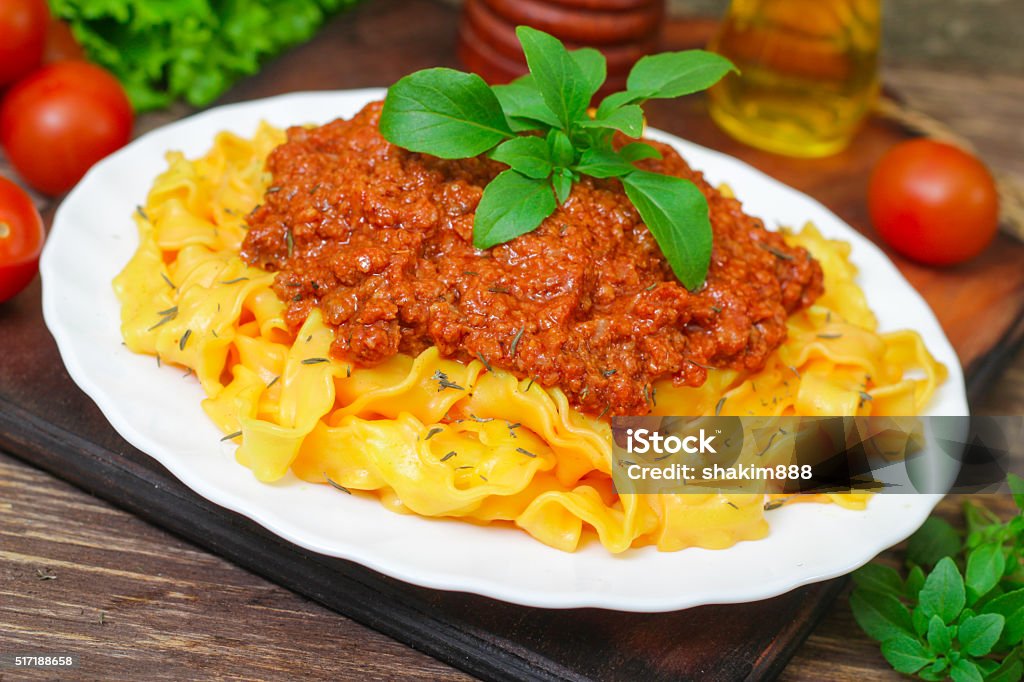 Traditional Italian pasta Bolognese or Bolognese with cooked pasta Traditional Italian pasta Bolognese or Bolognese with cooked pasta noodles topped with a spicy tomato based meat sauce garnished with fresh basil on a wooden background Basil Stock Photo