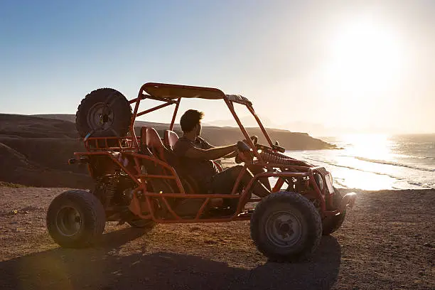Active man driving quadbike on dirt road by the sea in sunset.