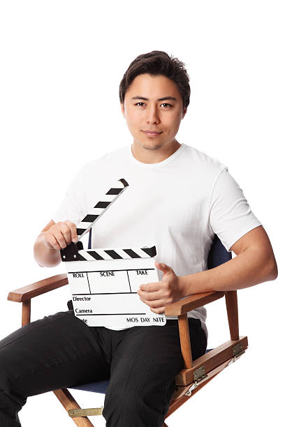 Young attractive man holding a film slate, wearing a white t-shirt. White background.