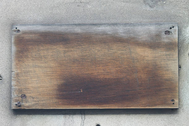 Old wooden plaque with metal screws and nails on a stone wall of a house