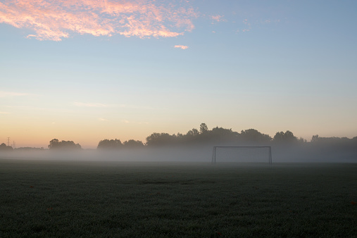 Early morning fog and sunrise on field with soccer goal