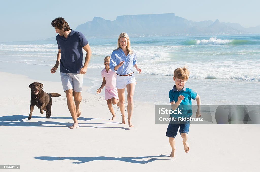 Family running with dog Family playing with pet on the beach. Happy beautiful family running at beach with pet dog. Smiling parents with son and daughter having fun at seaside. Dog Stock Photo