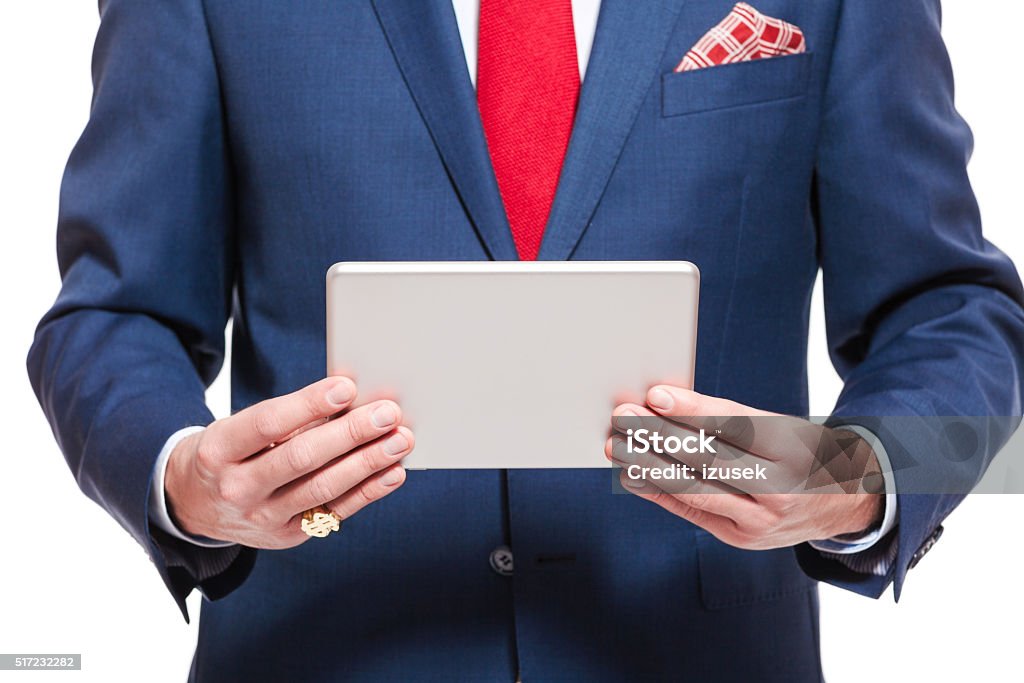 Elegant businessman wearing suit, holding a digital tablet Elegant businessman wearing suit, red tie and pocket square, holding a digital tablet. Close up of hands and torso, unrecognizable person. Studio shot, isolated on white. Adult Stock Photo