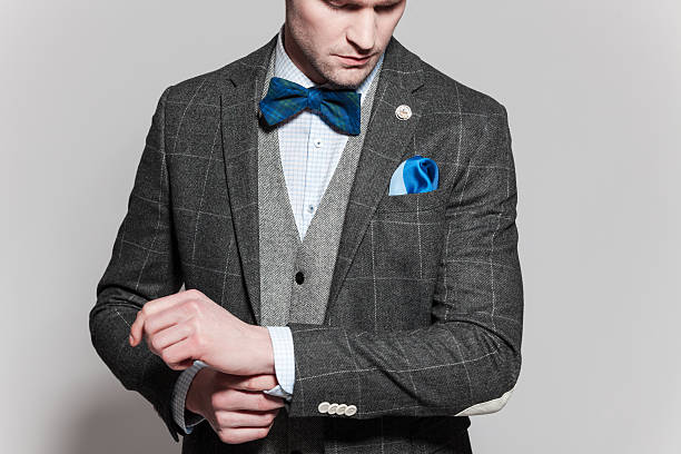 Old-fashioned elegance man wearing tweed jacket and vest Portrait of elegant businessman wearing tweed jacket, vest, bow tie and pocket square. Standing against grey background. Studio shot, one person. Tweed Suits stock pictures, royalty-free photos & images