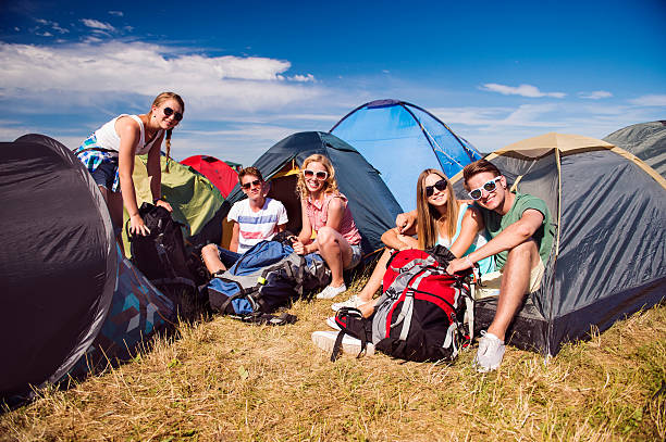 Teenagers sitting on the ground in front of tents Group of teenage boys and girls at summer music festival, sitting on the ground in front of tents, packing music festival camping summer vacations stock pictures, royalty-free photos & images