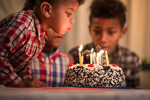 Black toddler blowing candles out. Black toddler blowing candles out. Child blows birthday candles out. Youngest brother's birthday. Spending festive time together. happy birthday cousin images stock pictures, royalty-free photos & images