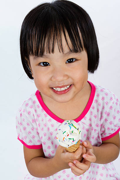 Asian Little Chinese Girl Eating Ice Cream Asian Little Chinese Girl Eating Ice Cream isolated on White Background asian little chinese girls eating ice cream stock pictures, royalty-free photos & images