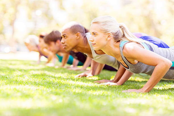 Friends Doing Push-Ups In Park Young woman with friends doing push-ups in bootcamp class in the park. Horizontal shot. military camp stock pictures, royalty-free photos & images