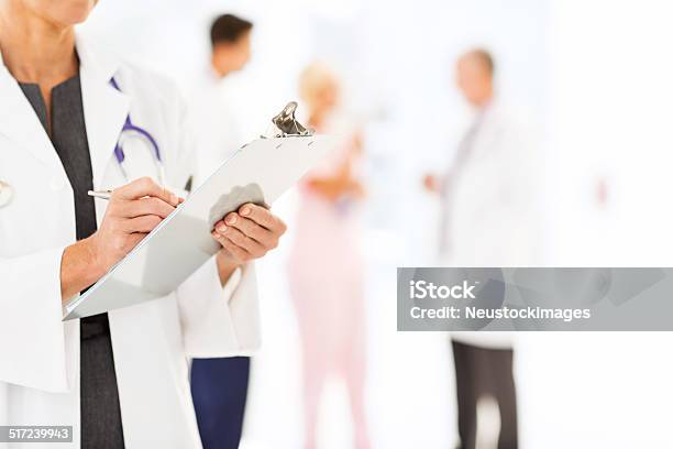Confident Female Doctor Writing On Clipboard In Hospital Stock Photo - Download Image Now