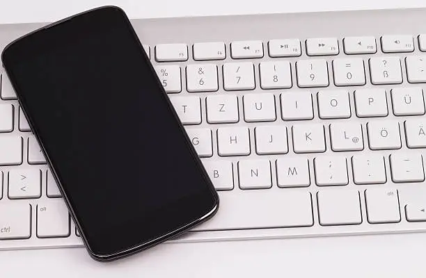 Image shows a smartphone on a keyboard, isolated on white background