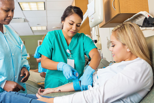 Nurse bandaging arm of patient after she donates blood 