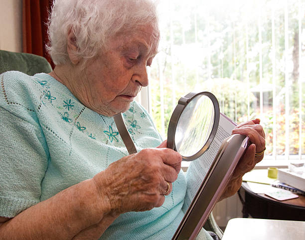 istock Elderly woman using a magnifier to read a book 517269039