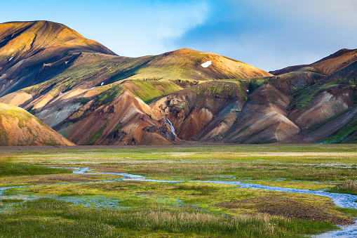 Green Valley is flooded with melt water. Snow lies in the hollows of colorful rhyolite mountains. Early summer morning in the National Park Landmannalaugar, Iceland