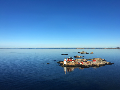 Rocky Island in a fjord of sweden, blue sky, blue calm water, red house and small lighthouse, very calm scene
